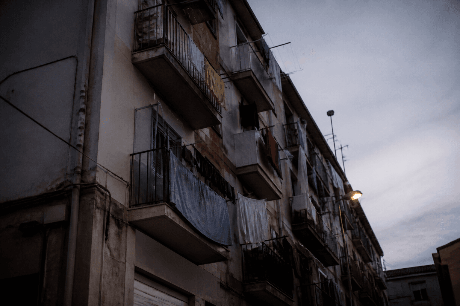 Laundry hanging from the balconies of a residential apartment block photographed from the street below at dusk.