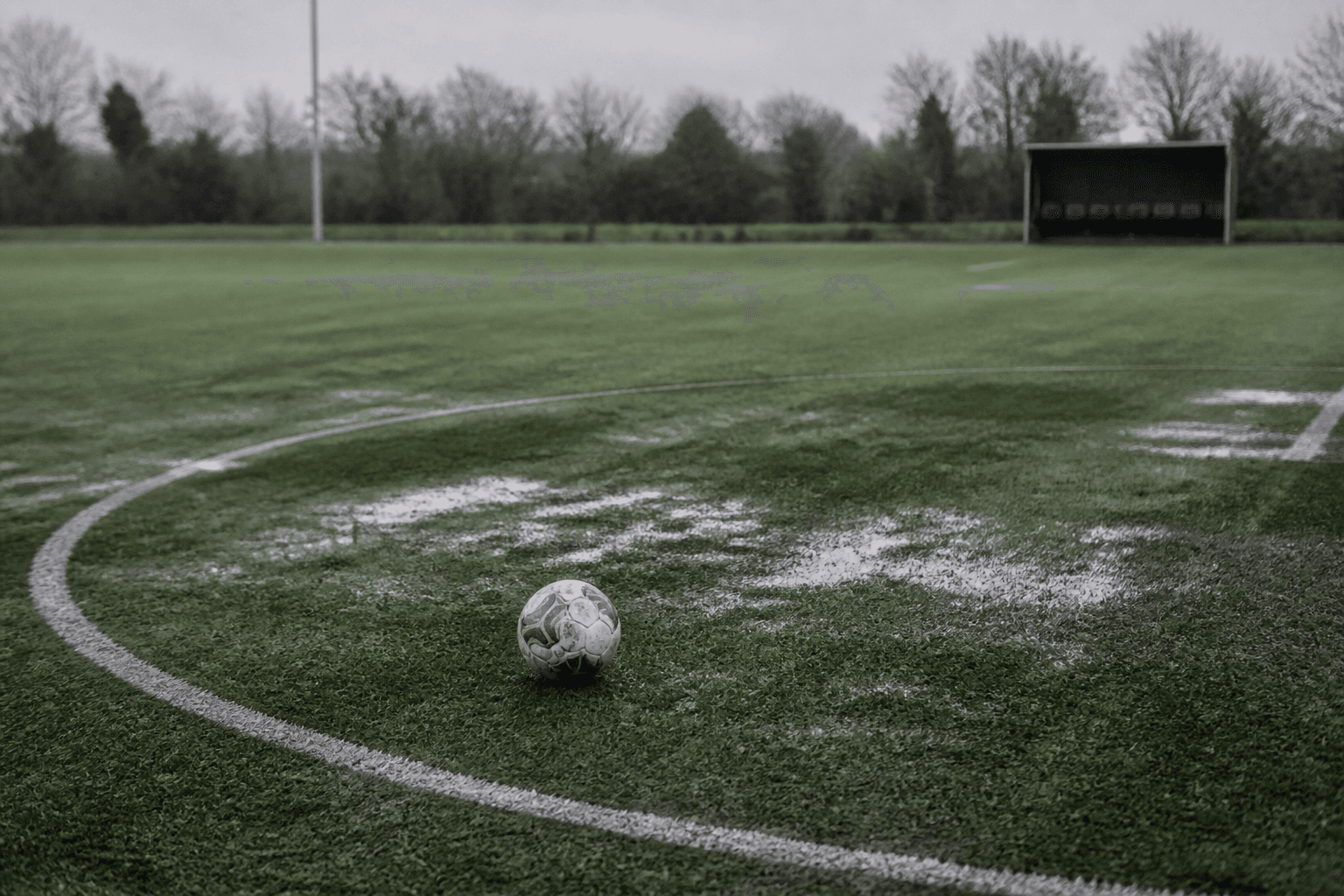 A lone football resting on the wet centre circle of an empty training pitch under grey morning light.