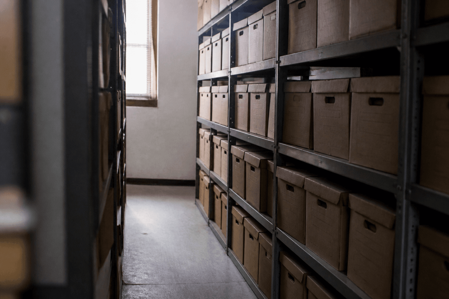 Cardboard archive boxes lined up on metal shelves in a dim courthouse records room.