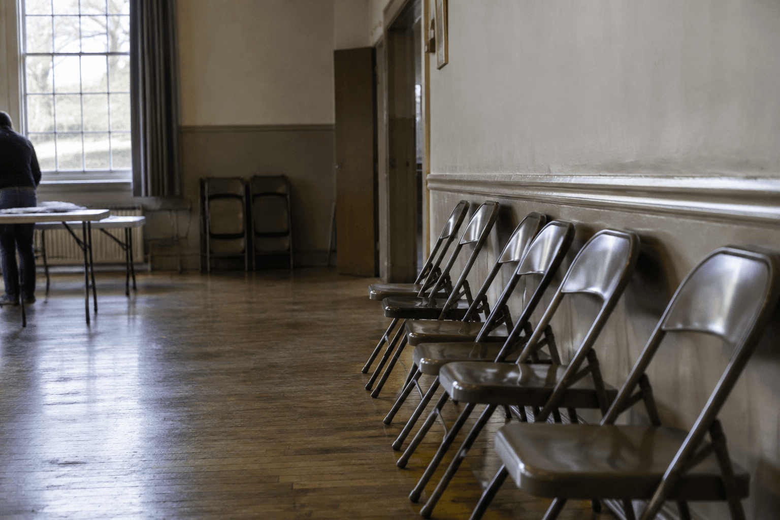 Empty folding chairs lined up against the wall of a plain community hall the morning after polling day.
