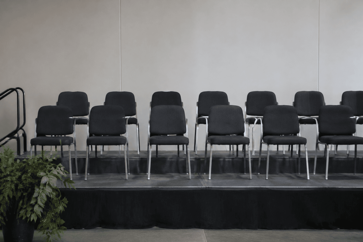 Rows of empty chairs on a stand against a plain backdrop where a group photo would have been taken.