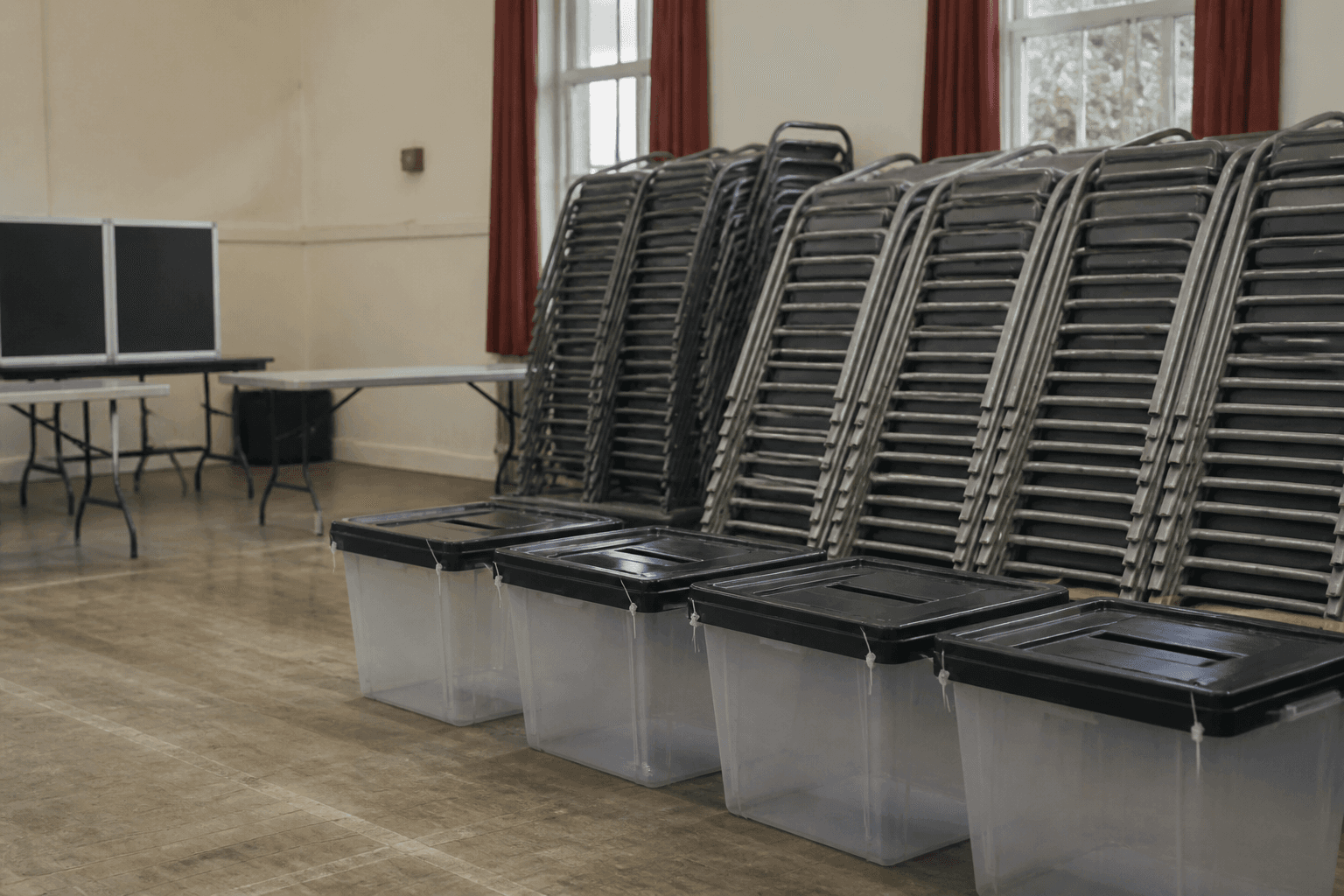Stacked folding chairs and empty ballot boxes in a school hall used as a polling station.