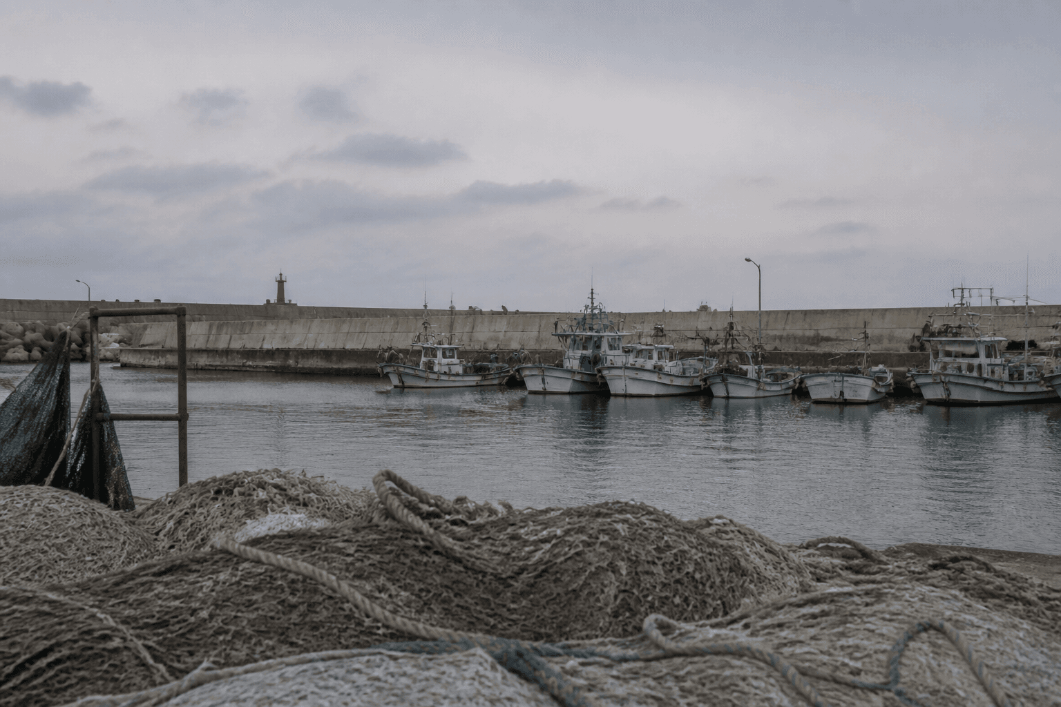 Fishing boats moored behind a breakwater in a quiet harbour on South Korea's east coast under an overcast morning sky.