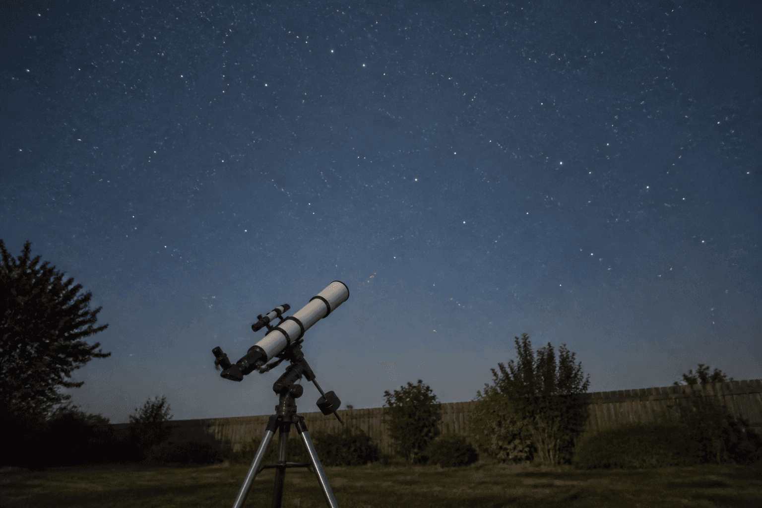 A backyard telescope on a tripod angled toward a clear, star-filled night sky away from city lights.