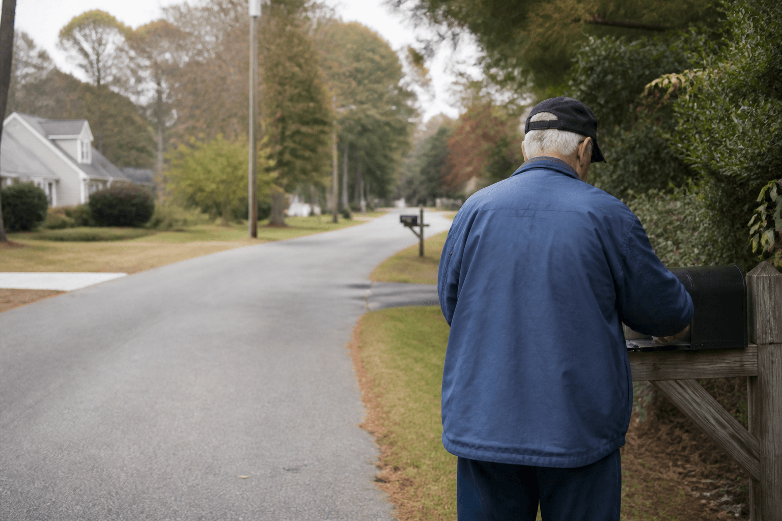 An older man seen from behind opening his home mailbox on a quiet residential street in the morning.